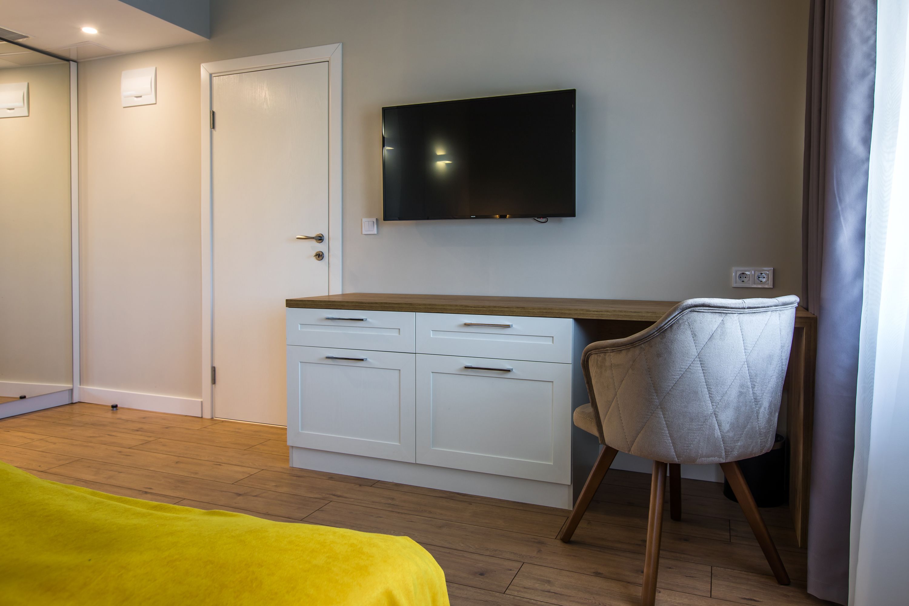A bedroom with a bed, a desk, a chair, a television, and a door.