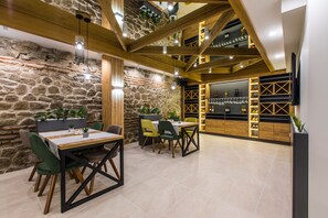 Un comedor con mesas y sillas de madera, una pared de piedra y una estantería para vinos con botellas.
