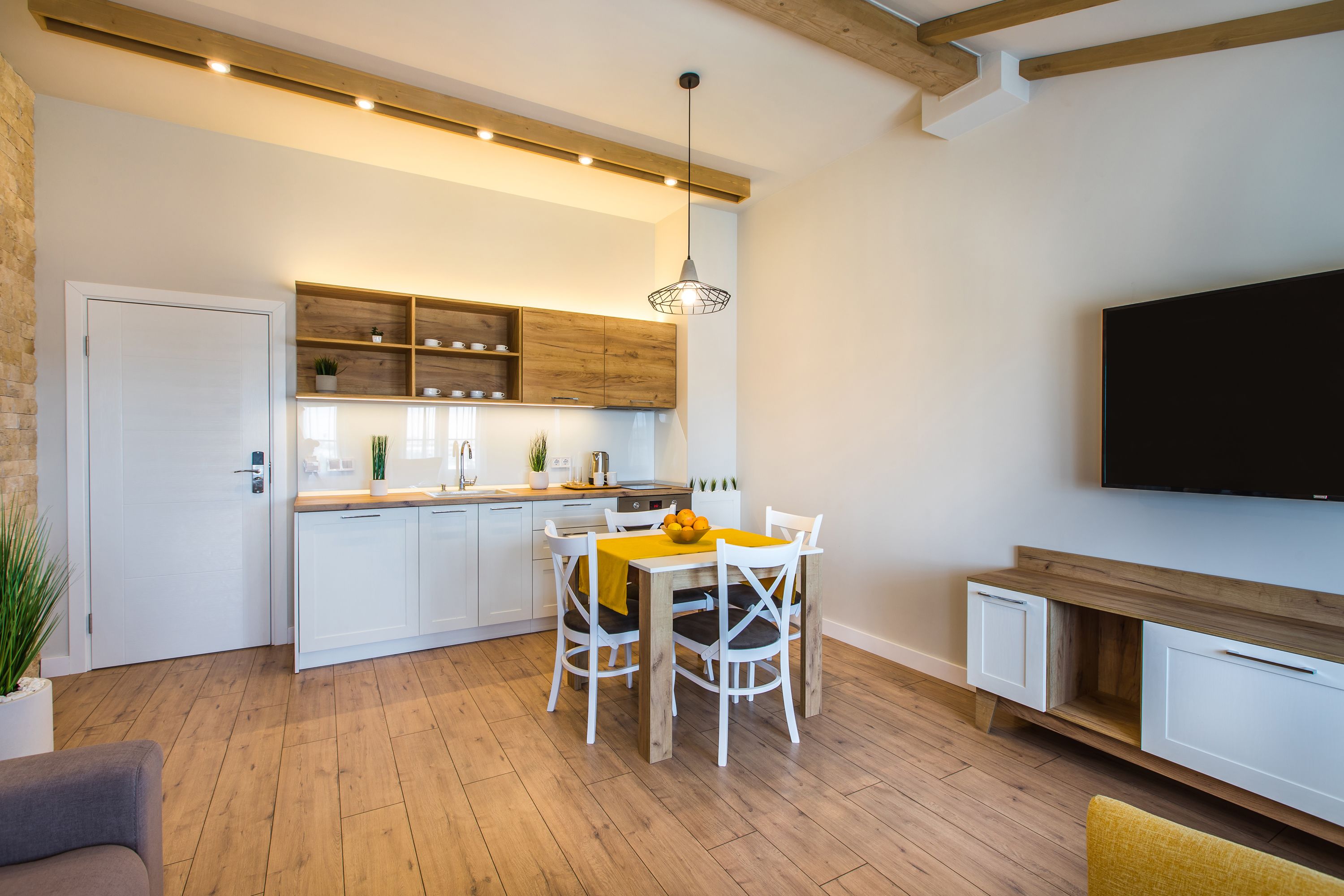A modern kitchen with white cabinets, wooden shelves, and a dining area with a table and chairs.