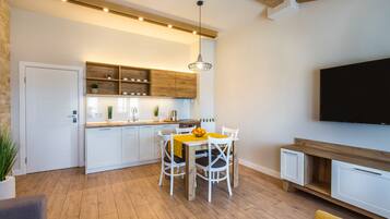 A modern kitchen with white cabinets, wooden shelves, and a dining area with a table and chairs.