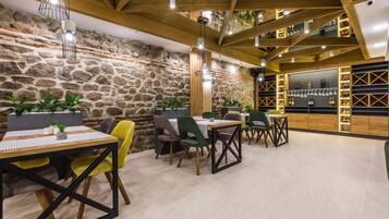 Restaurante com paredes de pedra, vigas de madeira e um bar com prateleiras cheias de garrafas e copos.