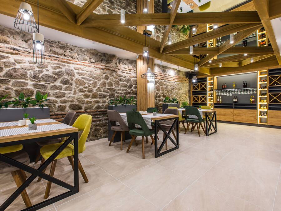 Restaurante com paredes de pedra, vigas de madeira e um bar com prateleiras cheias de garrafas e copos.