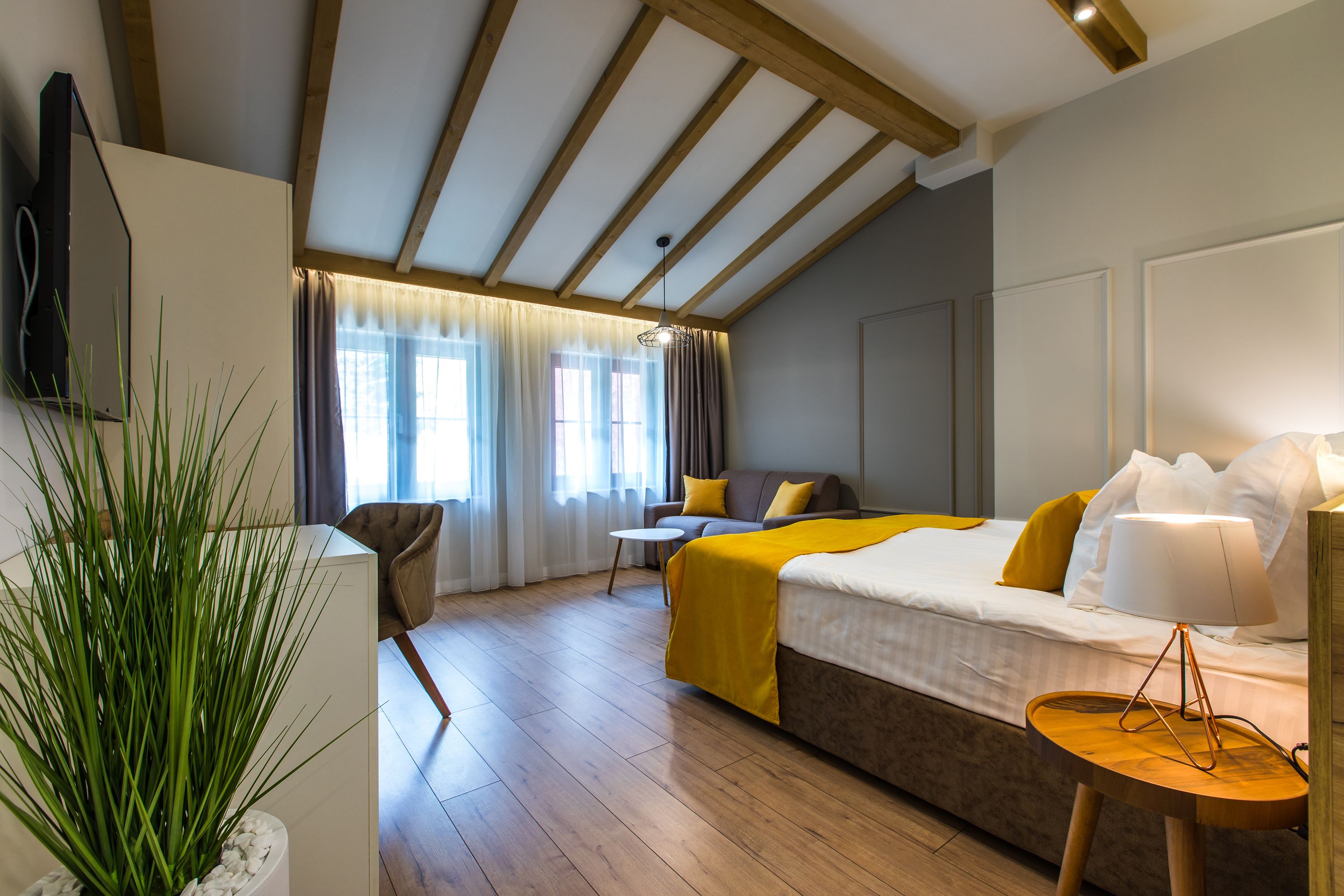 Ein modernes Hotelzimmer mit Holzboden, einem Bett mit gelber Bettwäsche, einem Nachttisch mit Lampe, einem Sessel und einem Topfpflanzen.