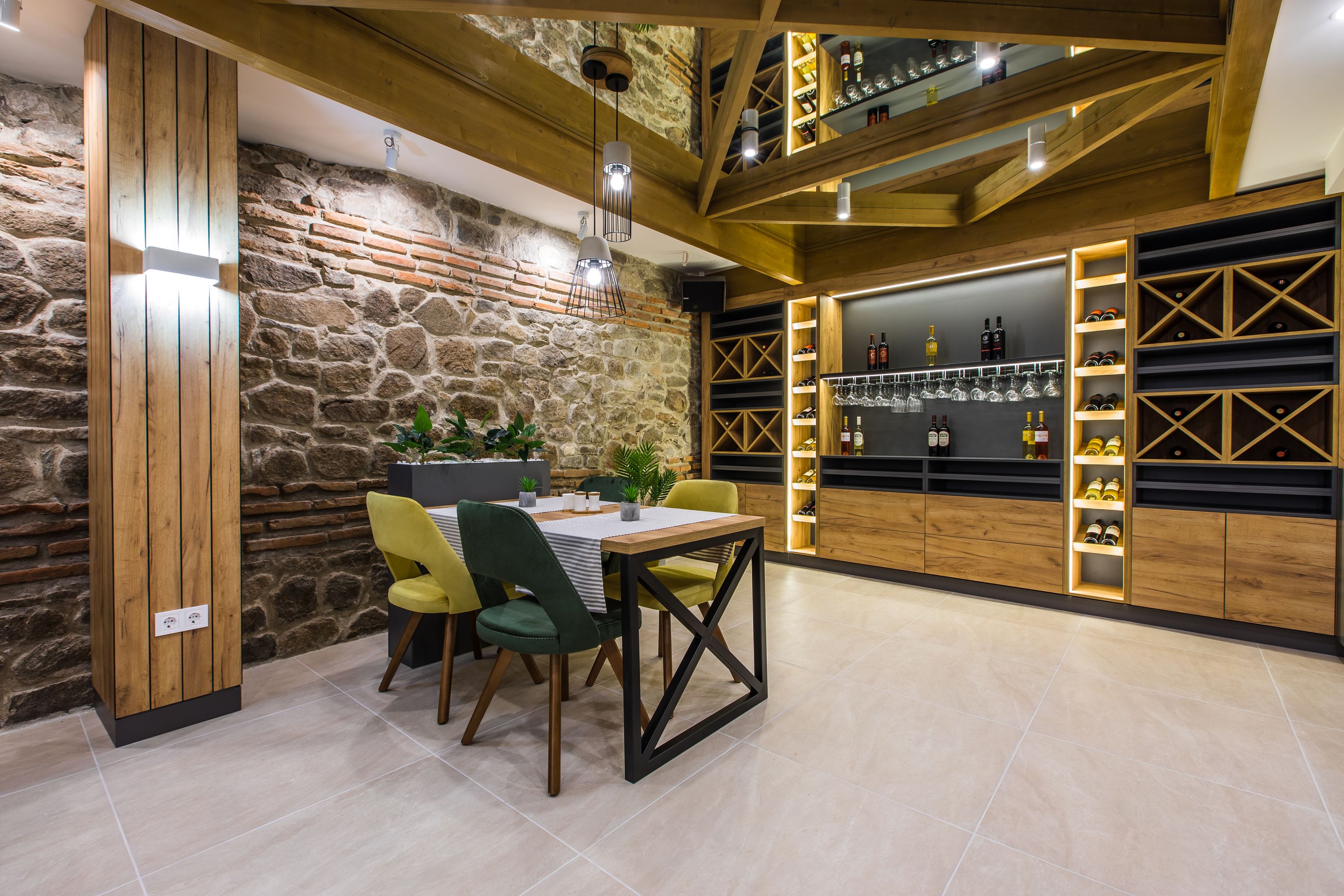 A dining area with a stone wall, wooden beams, and a wine rack with bottles.