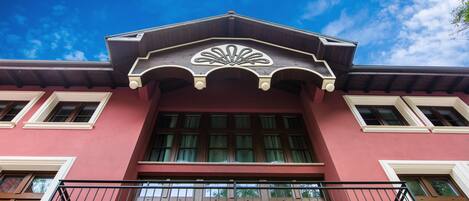 A building with a red facade, large windows, and a balcony with ornate metal railings.