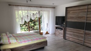 A bedroom with a bed, a TV, a wardrobe, and a small table with books and a glass bowl.