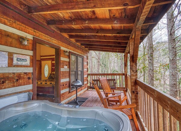 Una cabaña de madera con jacuzzi, terraza de madera y vistas al bosque.