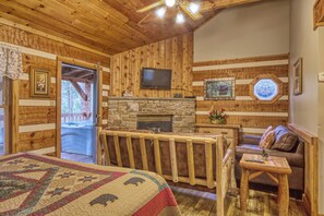 Una habitación acogedora con chimenea de piedra, paredes de madera, televisor y un rincón de estar confortable.