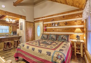 A cozy log cabin room with a large bed, wooden walls, a kitchen area, and a rustic decor.