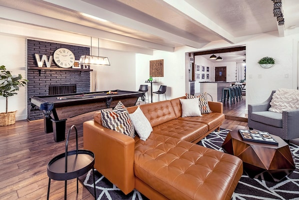 Una sala moderna con mesa de billar, sofá de cuero y un rincón de estar acogedor.