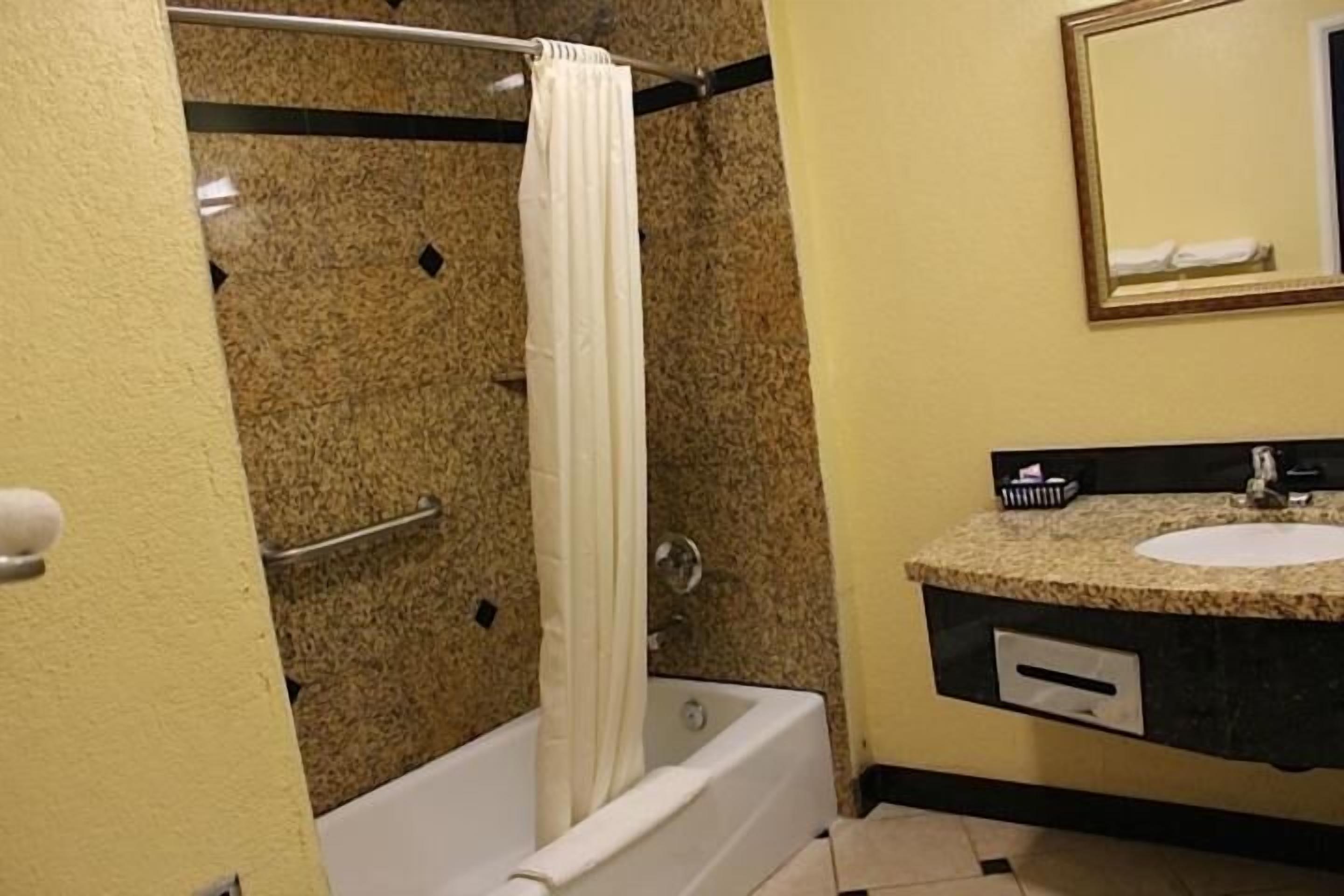Een badkamer met een bad, douchegordijn, wastafel en spiegel.