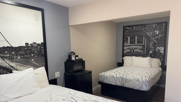 Una camera d'albergo con un letto, un comodino, un forno a microonde e un murale raffigurante un panorama urbano.