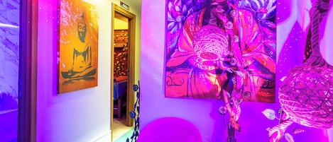 A room with a pink chair, a table with a lamp, and a painting on the wall.