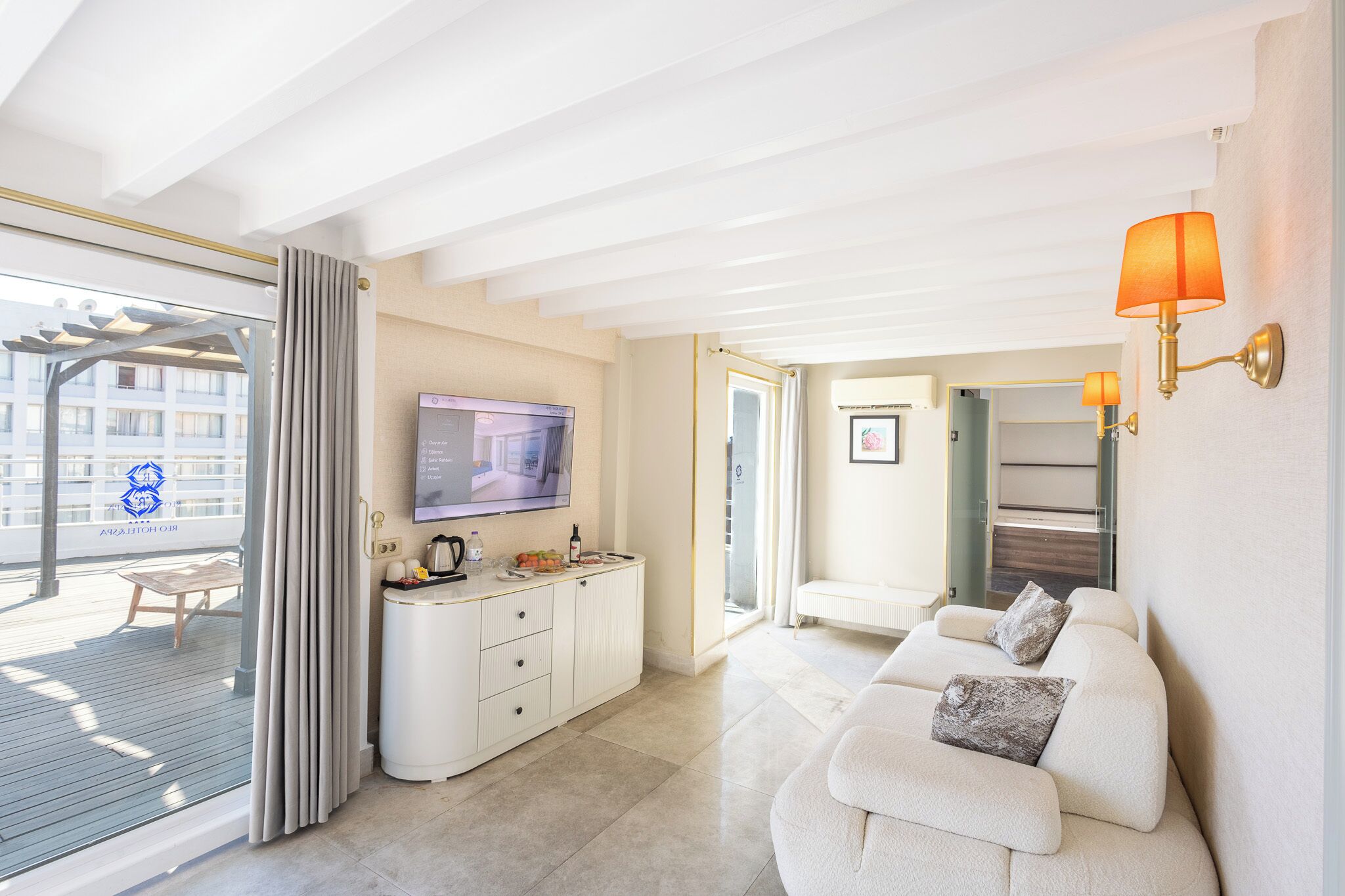 Une chambre d’hôtel moderne dotée d’une télévision, d’une kitchenette, d’un coin salon et d’un balcon offrant une vue sur la ville.