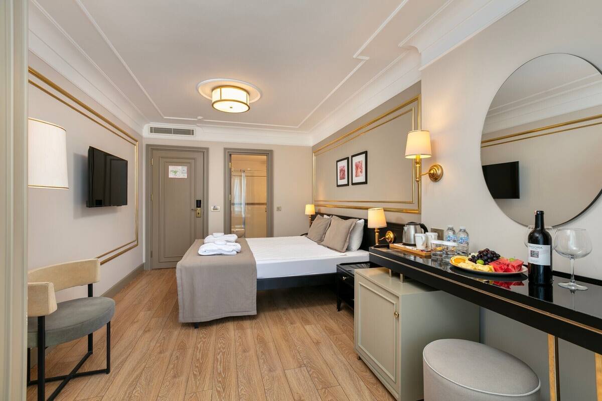 A hotel room with a bed, a small desk with a mirror, a TV, and a minibar.