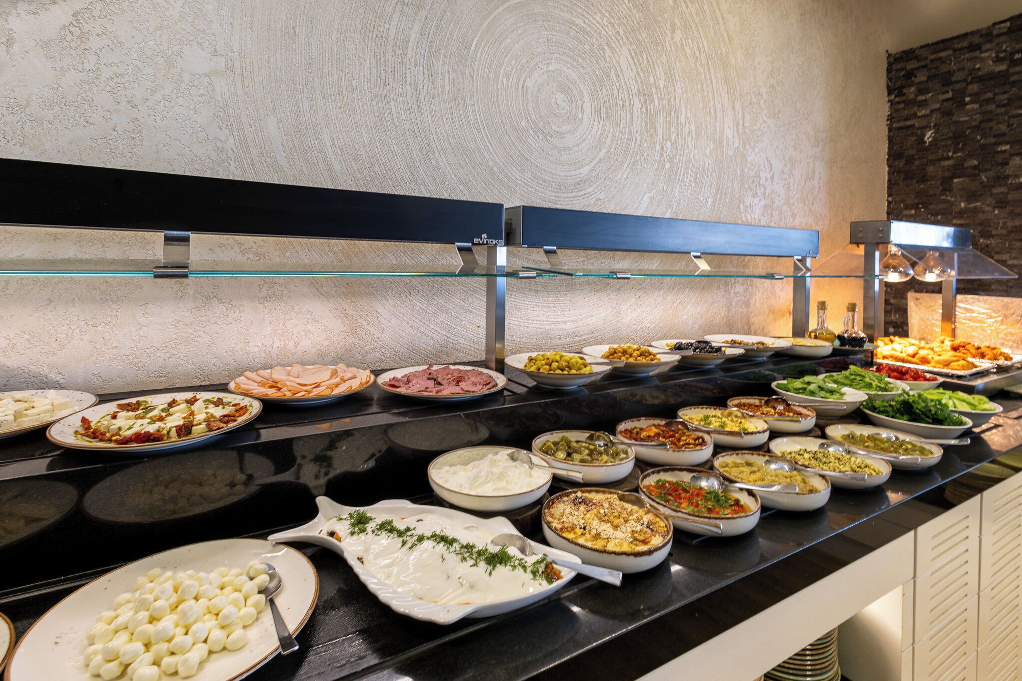 Un buffet proposant divers plats, un plan de travail noir et un mur en bois.