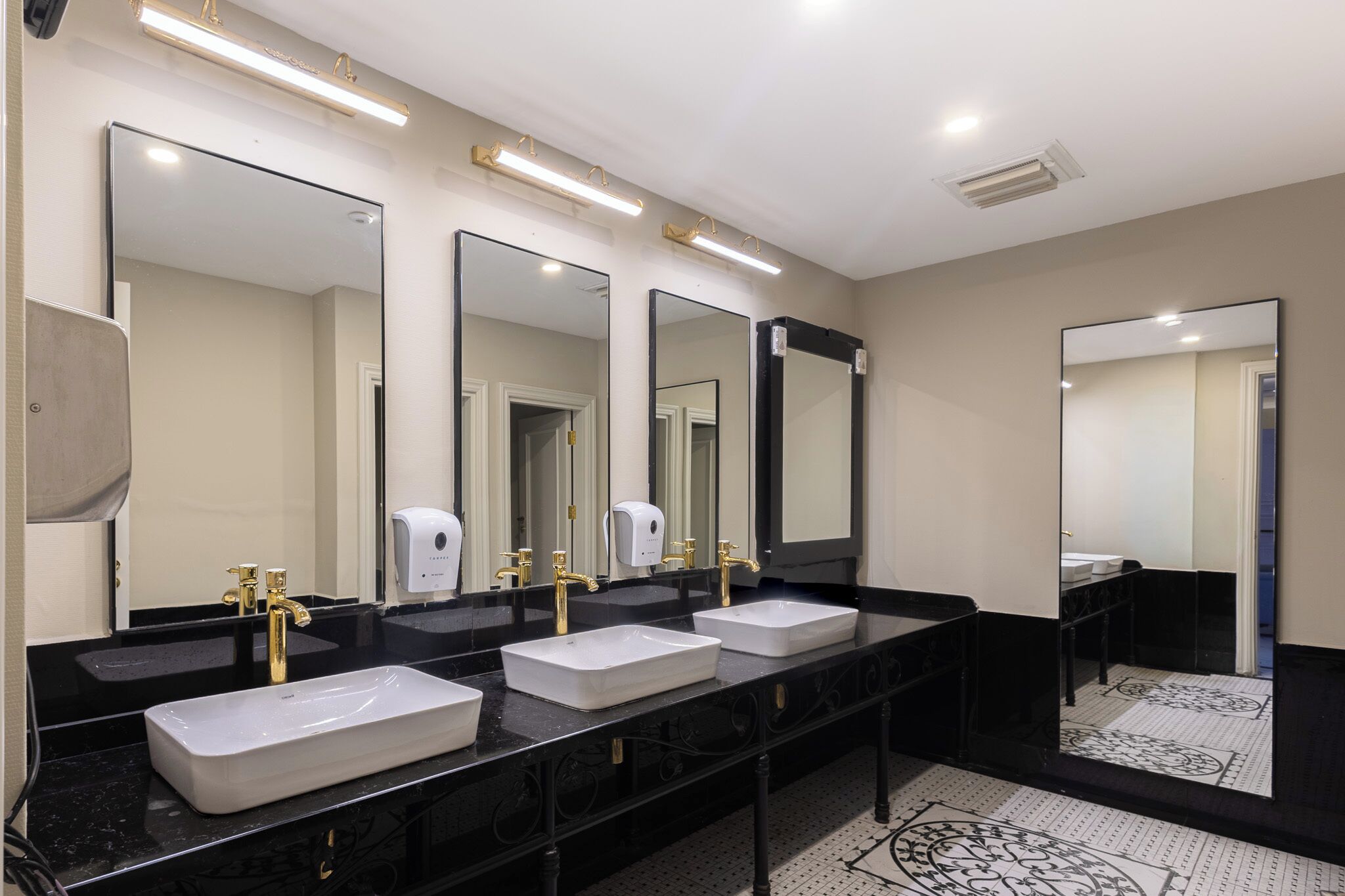 A hotel bathroom with three sinks, black countertops, gold faucets, and large mirrors.