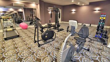 Ein Fitnessraum eines Hotels mit Cardiogeräten, Gewichten und einem gemusterten Teppich.