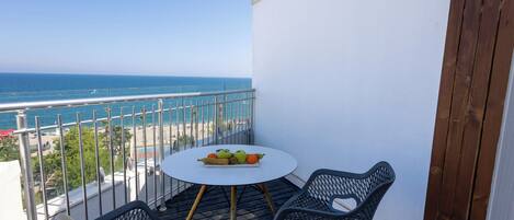 A balcony with a table and chairs, a view of the sea, and a beach in the background.
