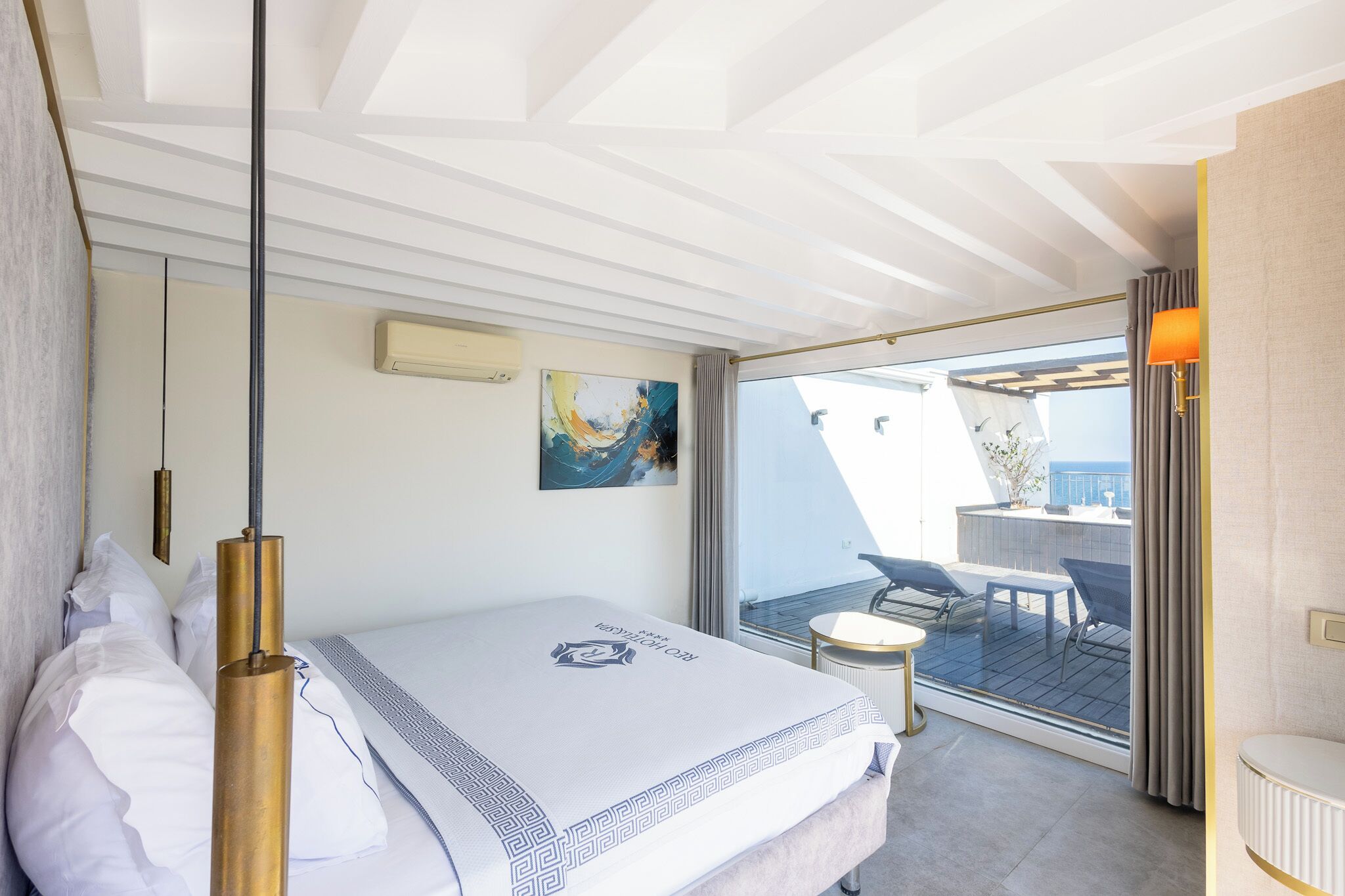 A modern hotel room with a bed, a small table, a chair, a balcony with a table and chairs, and a painting on the wall.