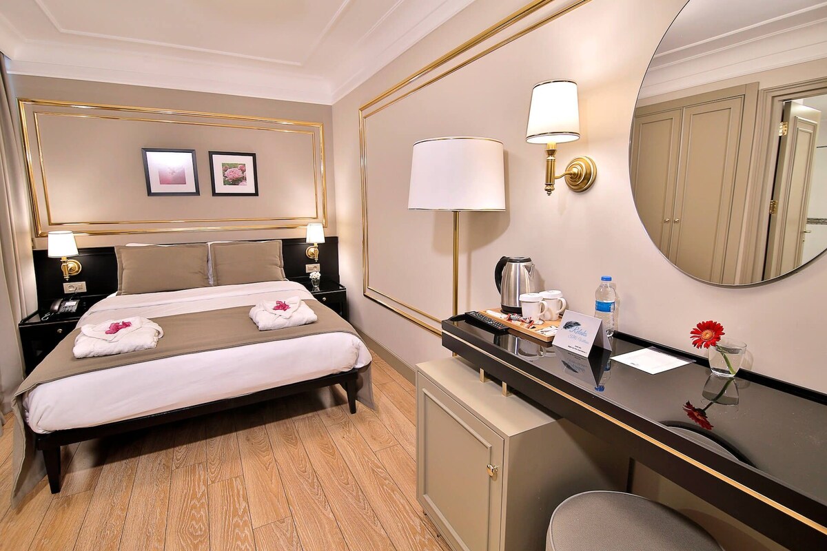 A hotel room with a bed, bedside tables, a desk with a mirror, and a small cabinet.