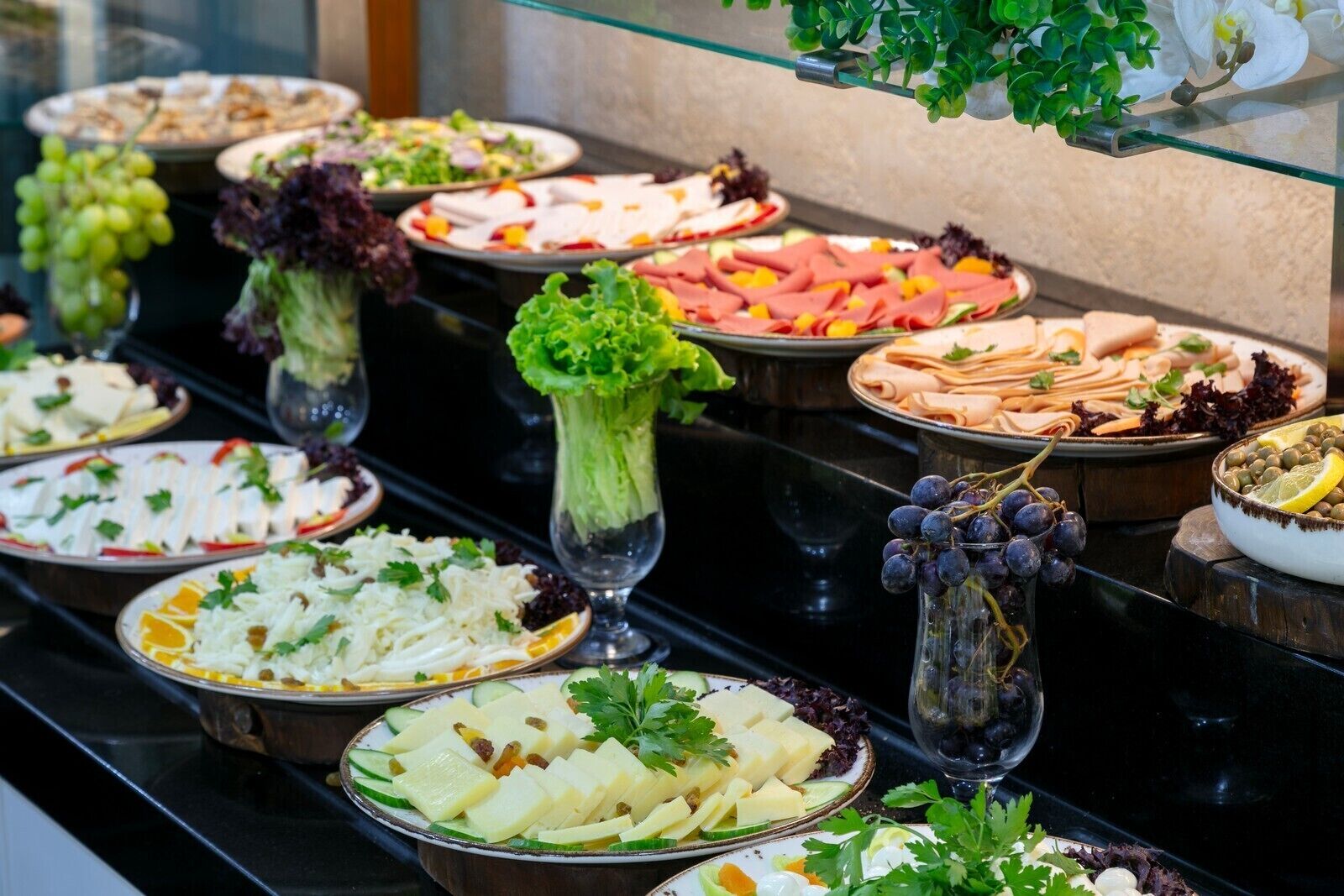 Un bufé con diversos platos, entre ellos ensaladas, carnes y quesos.