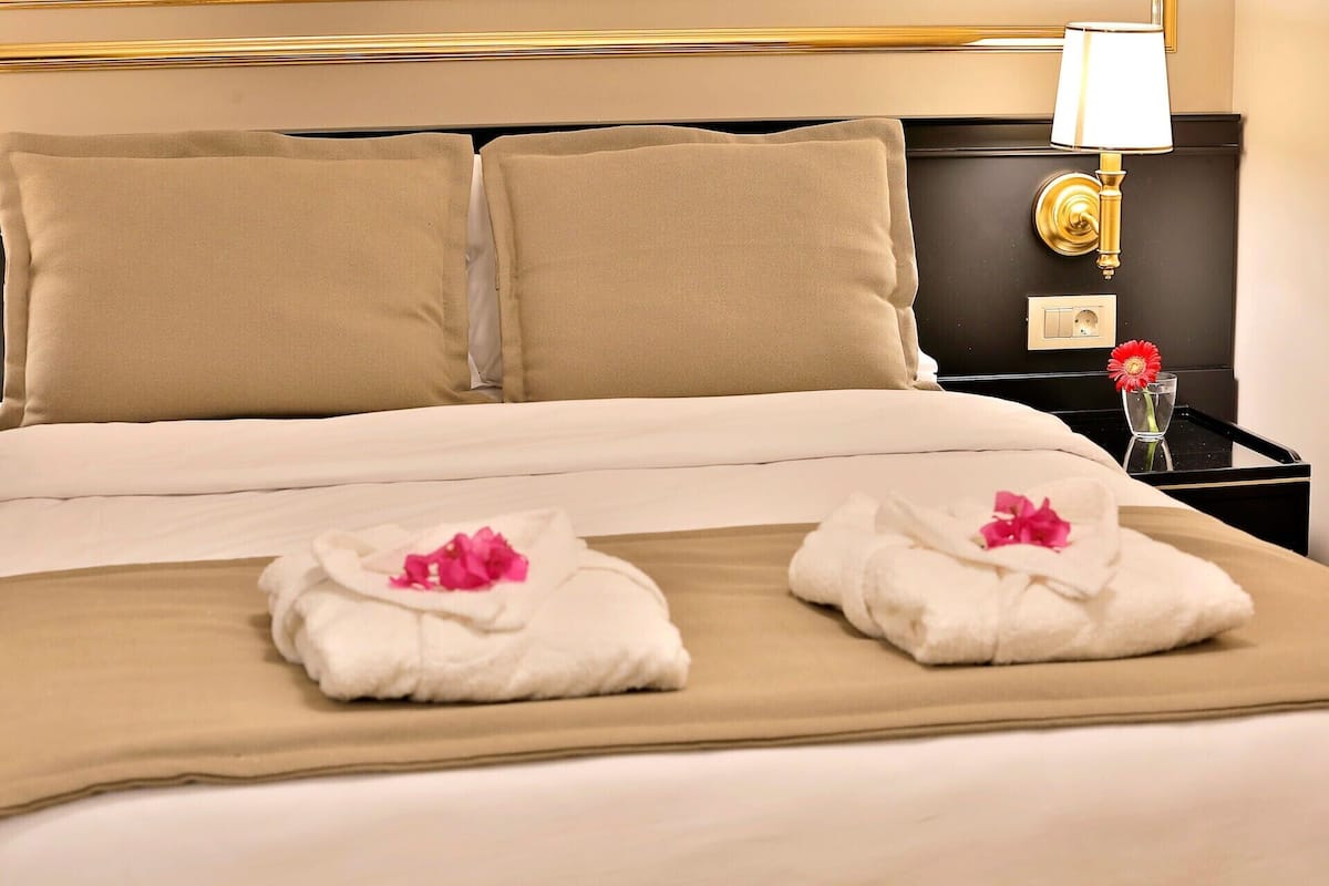A hotel room with a bed, two pillows, a nightstand with a lamp, and two towels with flowers.
