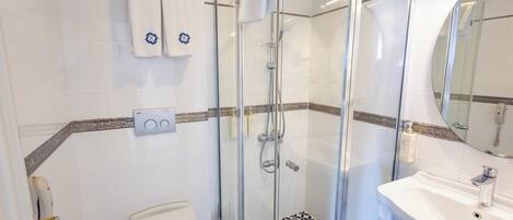 Ett modernt badrum med en dusch som är avskärmad med glasväggar, ett vitt handfat och en toalett.