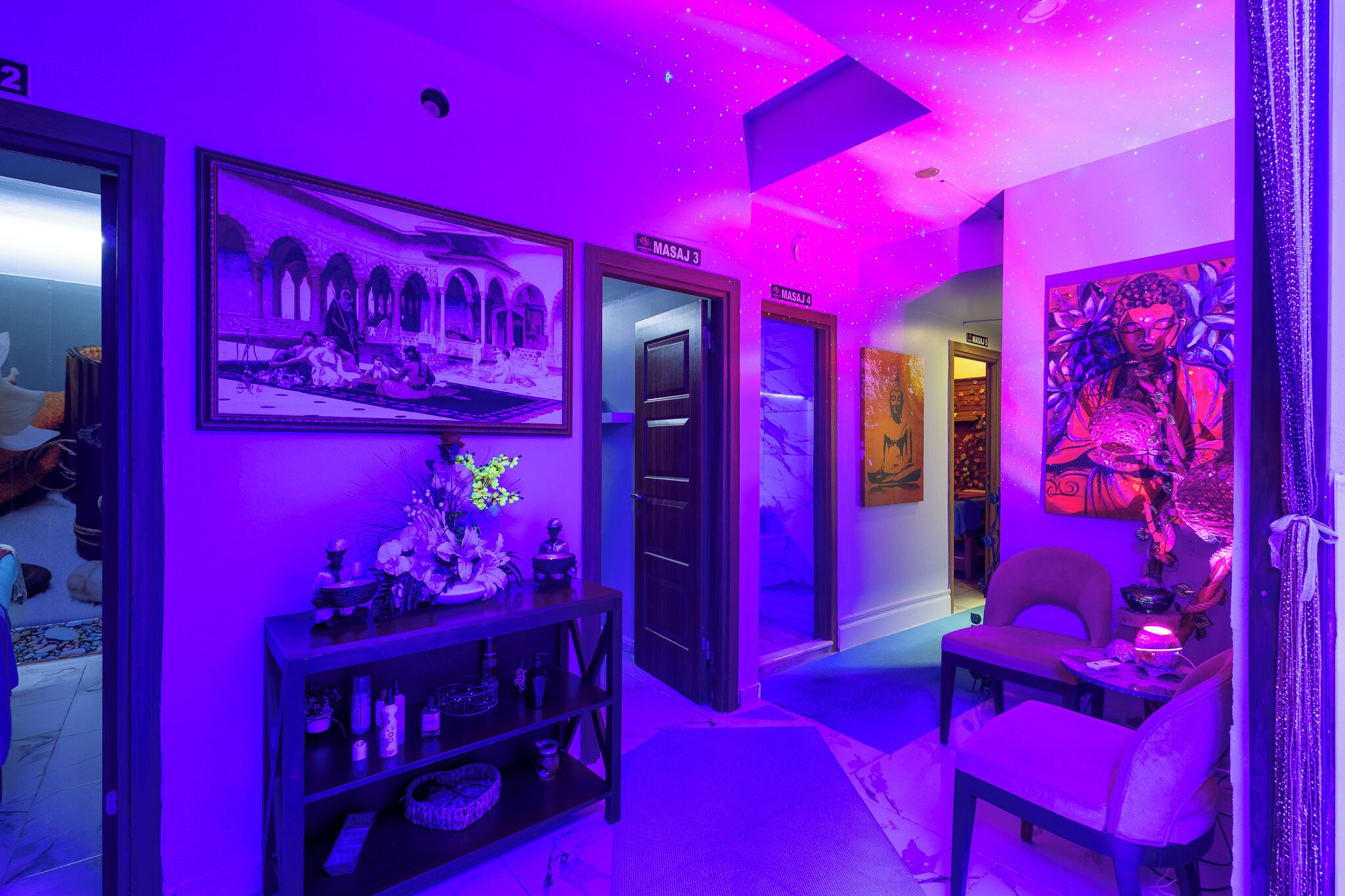 A hallway with purple lighting, a framed picture, a shelf with items, and a chair.