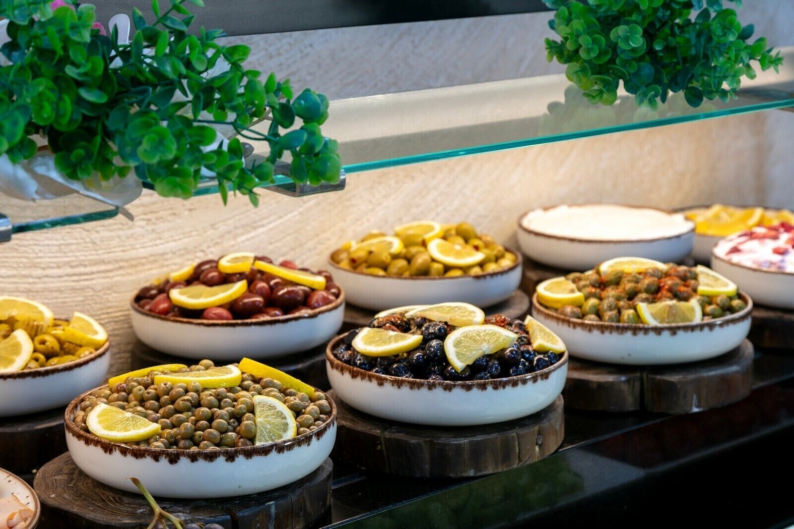 Ein Buffet mit verschiedenen Speisen, darunter Oliven, Bohnen und Früchte, auf einer Holztischplatte angerichtet.