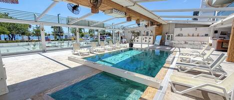 A pool area with lounge chairs, a smaller pool, and a covered seating area with a view of the sea.