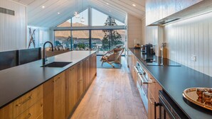 Una cocina moderna con una isla grande, armarios de madera y vistas a montañas a través de amplios ventanales.