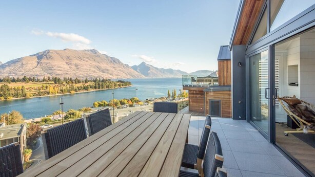 Un área de comedor al aire libre moderna con vistas a un lago y montañas.