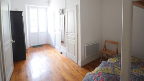 Ein Zimmer mit Holzboden, weißen Wänden, einem Bett mit floralem Bettzeug, einem Sessel und einer Heizung.