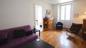 Ein Wohnzimmer mit einem violetten Sofa, einem Holzkabinett, einem blauen Sessel und einem kleinen Tisch.