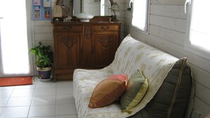 Une pièce comprenant une commode en bois, un miroir, une plante en pot, un canapé avec des coussins à motifs et une fenêtre avec des stores.
