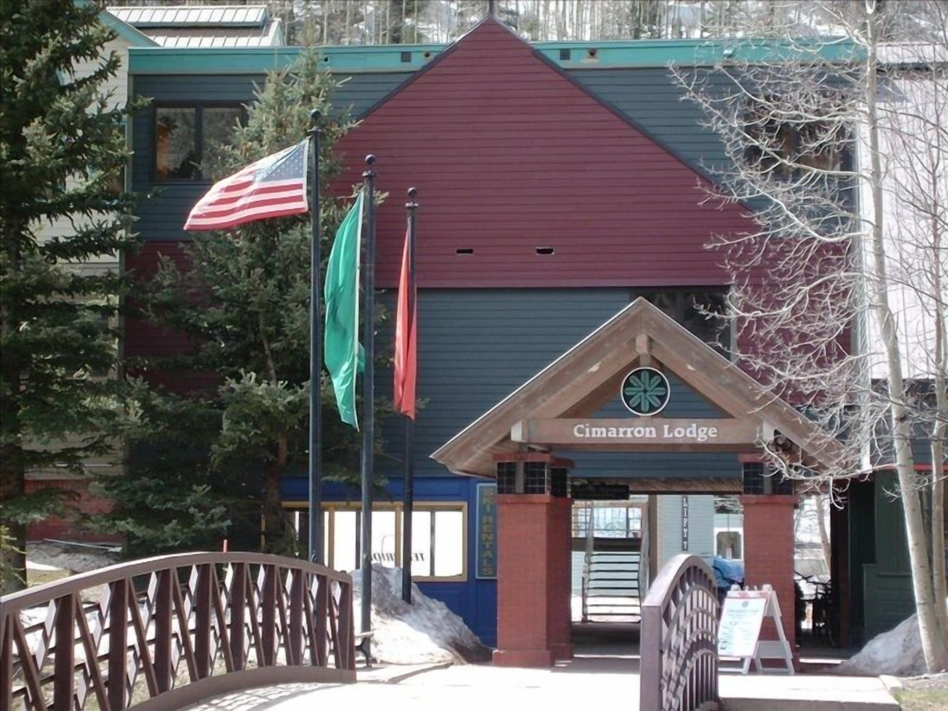 A lodge entrance with a red roof, American and Canadian flags, and a sign reading "Cimarron Lodge".