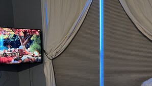 Een slaapkamer met een bed, een televisie aan de muur en een raam met gordijnen.