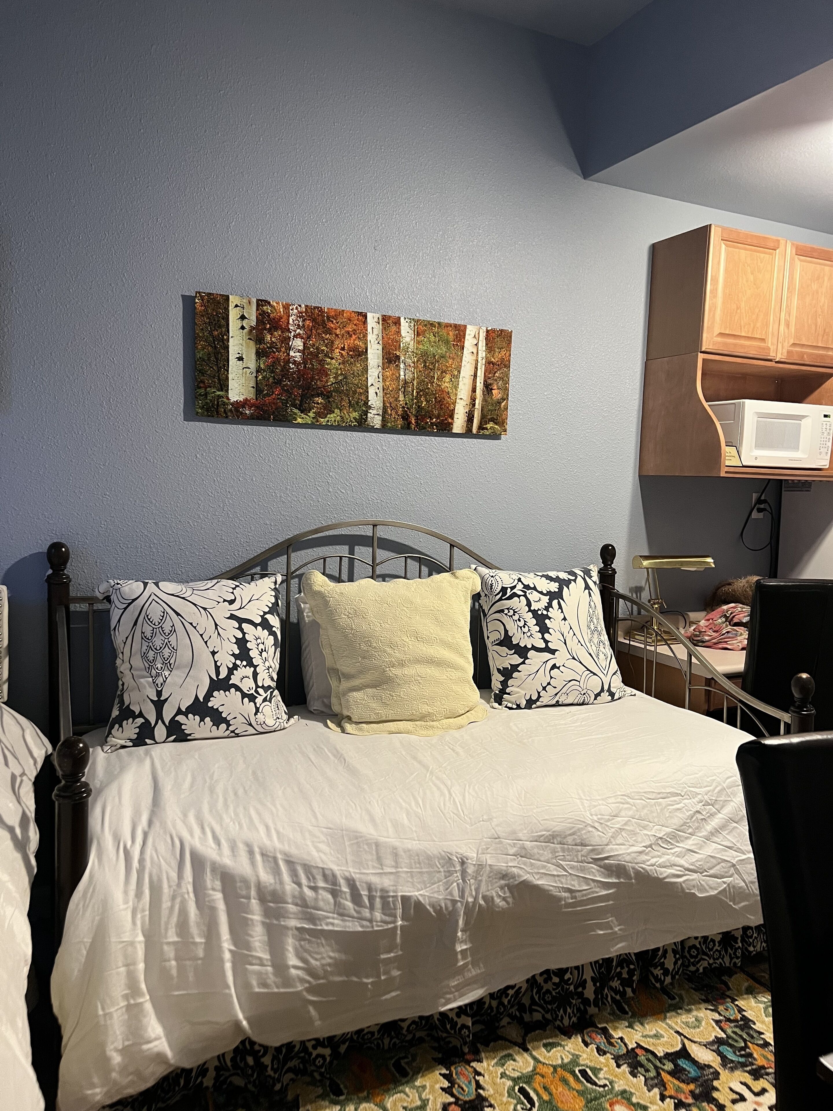 A bedroom with a bed, a nightstand, a lamp, and a wall-mounted microwave.