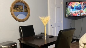 Een eetgedeelte met een donker houten tafel, zwarte stoelen, een geweven spiegel, een decoratieve vaas en een kleurrijk vloerkleed.