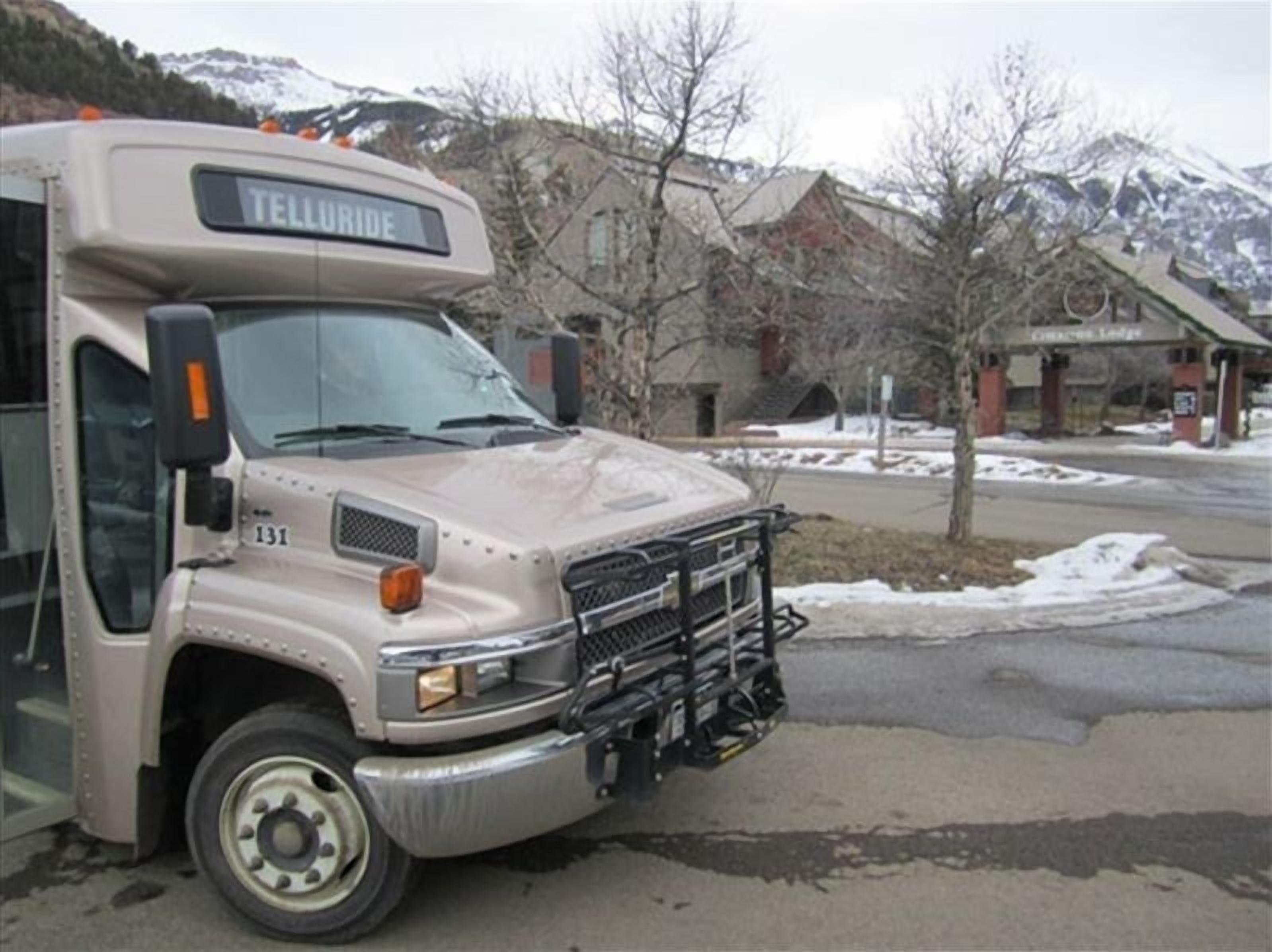 A bus with the word "TELLURIDE" on the front, parked in a snowy area with mountains in the background.