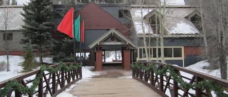 A wooden bridge leading to a building with a red roof and a small porch.