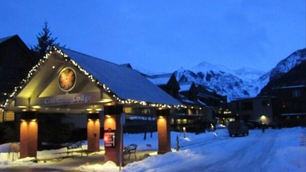 Een lodge met een met sneeuw bedekte dak en verlichte ingang, omgeven door bergen.