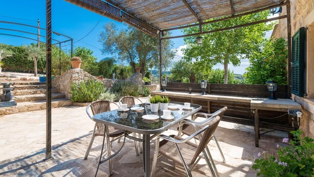 An outdoor patio with a table and chairs, a pergola, stone steps, and a view of the landscape.
