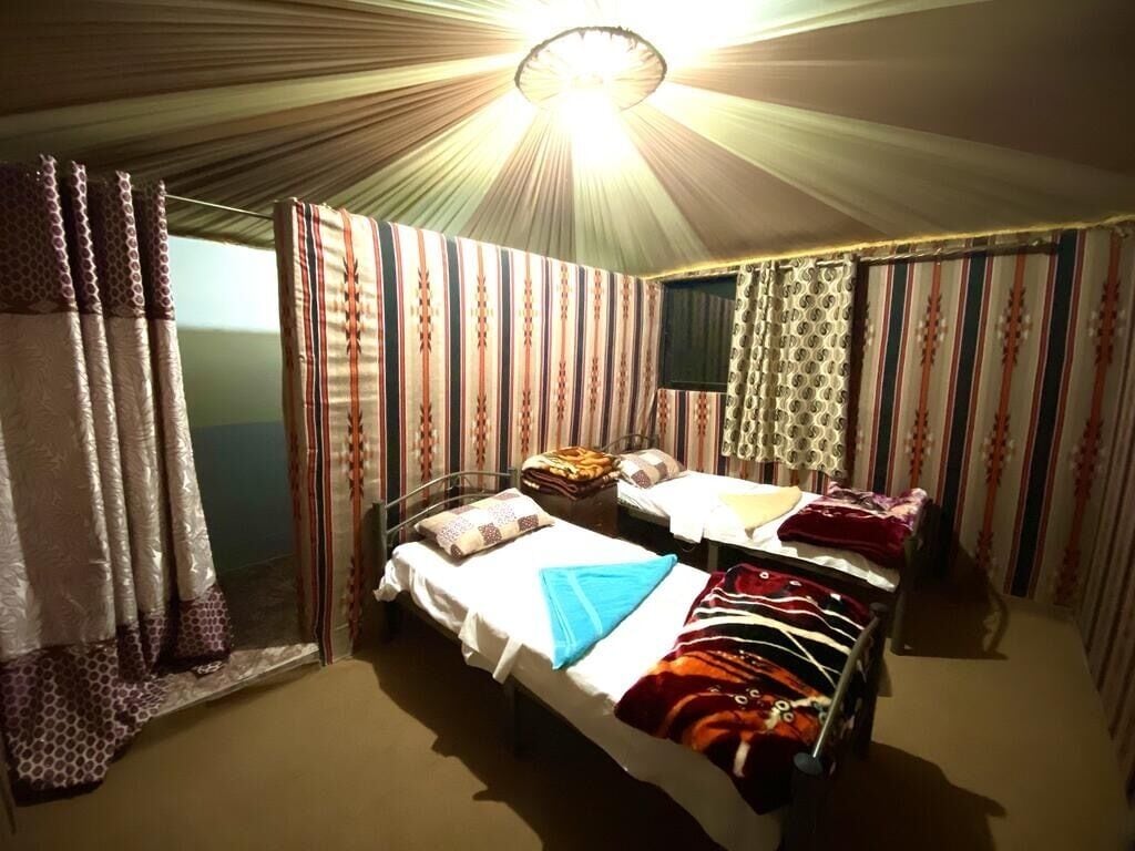 A single bed with a white sheet and a blue towel, a bedside table with a lamp, and striped curtains.