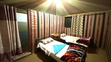 A single bed with a white sheet and a blue towel, a bedside table with a lamp, and striped curtains.