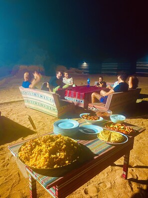 A group of people seated on a beach at night with a table set with food and drinks. - Wadi Rum Memories Camp (Wadi Rum)