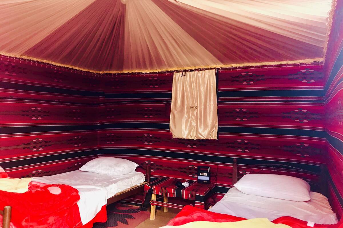 Une chambre avec deux lits, un baldaquin et un mur orné de motifs.