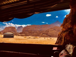 A desert landscape with mountains, a small building, and a rustic interior with a couch and a table. - Wadi Rum Memories Camp (Wadi Rum)