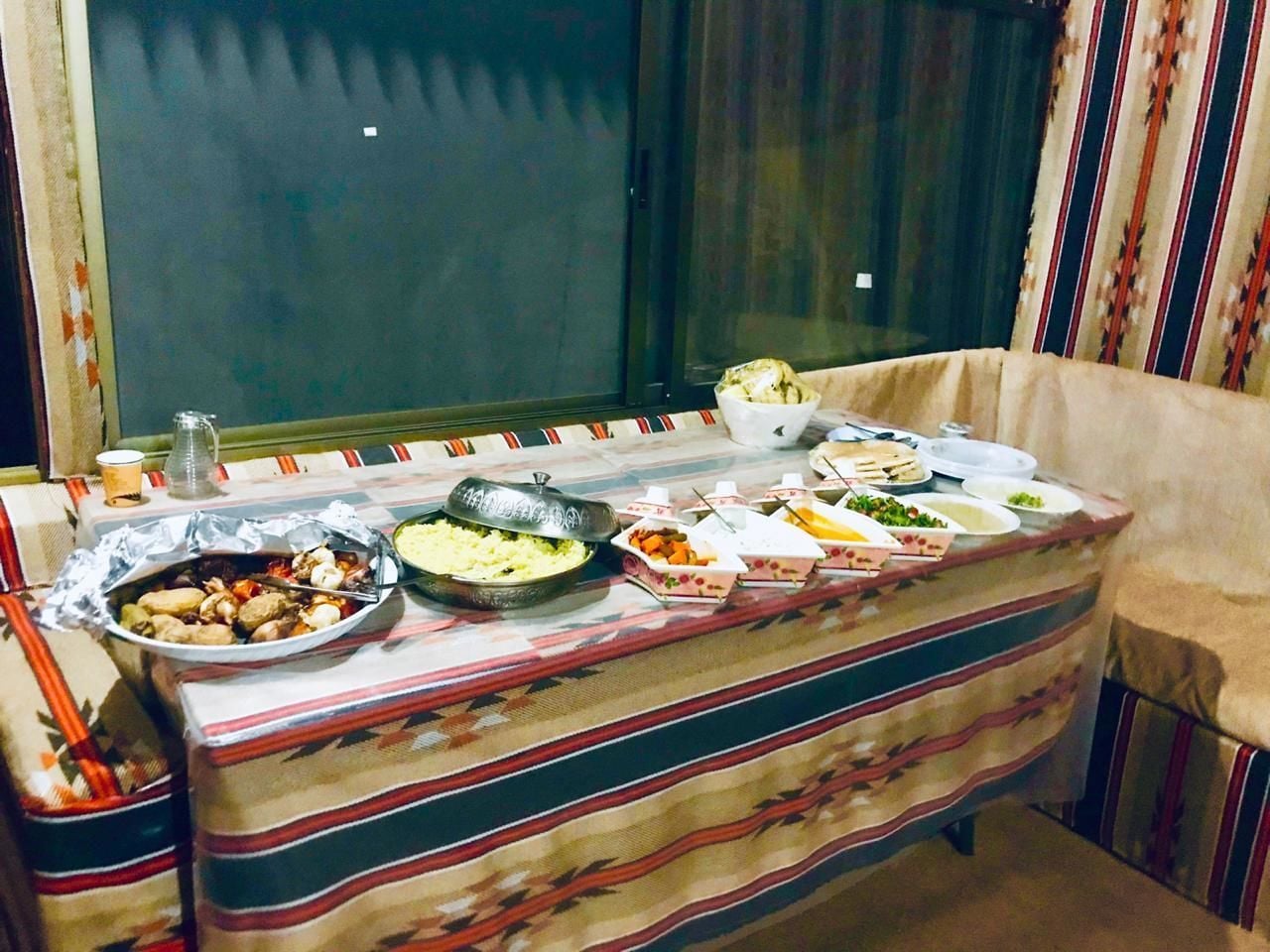 A dining table set with various dishes, a window with curtains, and a patterned tablecloth.